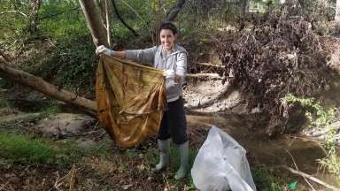 A smiling volunteer cleaning up a stream in Raleigh.