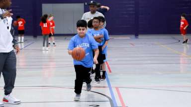 A group of kids playing basketball while a young boy dribbles the ball 