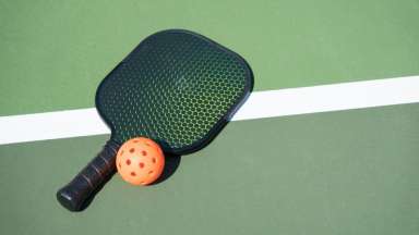 Pickleball paddle and ball laying on a court stripe