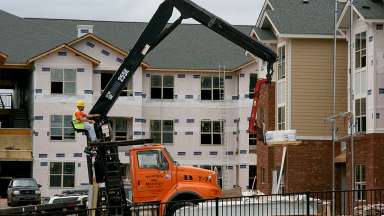 Man on crane moving lumber in an apartment construction site.