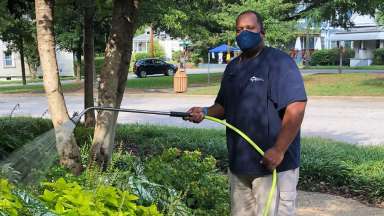 Man holding sprinkler over green bushes