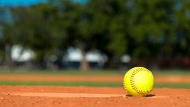 Softball sitting on the dirt on a softball field