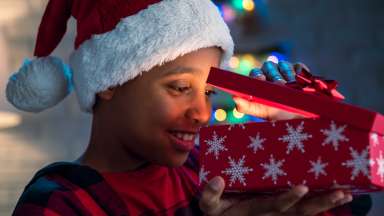 child in holiday hat opening a present