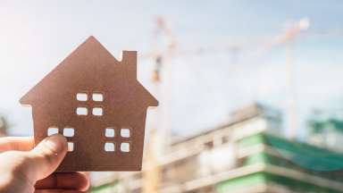 Miniature house model held in forefront of image; construction in background