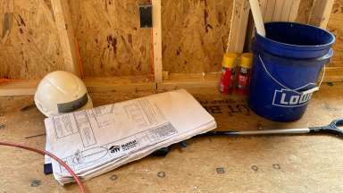 Image of hardhat, bucket, building plans, and other items sitting on the floor in an unfinished home