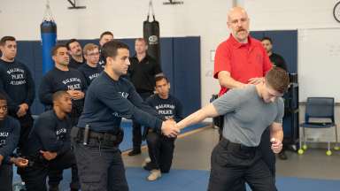 Raleigh Police recruits watching as two recruit practice grabbing a suspect while teacher overlooks