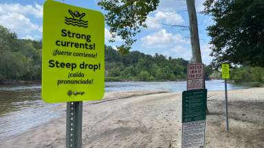 Image with the Neuse River in the background. The focus of an image is a safety sign that says &quot;Strong Currents! Steep Drops!&quot;