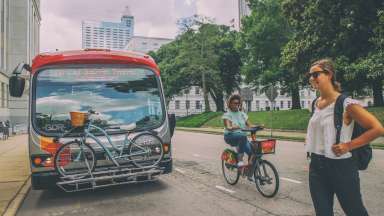 person walking, another biking, in front of a bus