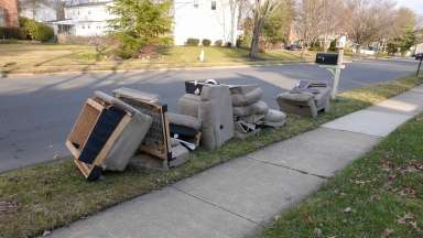 A discarded sofa sitting curbside on a neighborhood street with a sidewalk and mailbox in view.