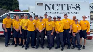 fourteen firefighters who are members of the Urban Search and Rescue team are standing in front of an NCTF truck