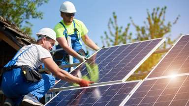 Two workers install solar panels on a roof.