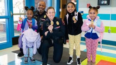 Two police officers posing with 3 children at a school. All holding a police shield sticker