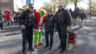 Three Raleigh police officers and the Grinch pose for a photo. A German Shepard K-9 dog stands next to an officer with a toy Santa riding on the dogs back.