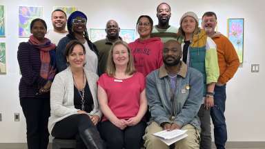 A group of 12 people smiling for the camera in an artsy setting.