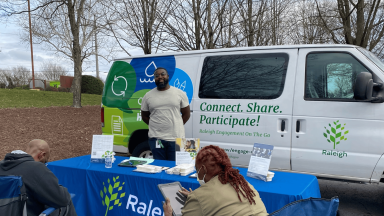 Staff member stands in front of engagement van while two people take surveys.