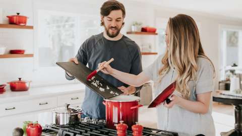 couple cooking with man putting cut onions into a pot