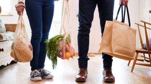 Close Up Of Couple Returning Home From Shopping Trip Carrying Groceries In Plastic Free Bags