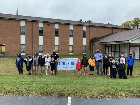 Large group standing outside with a faith and blue banner between them