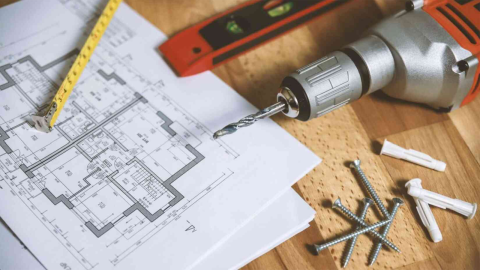 Image of plans, ruler, level, drill and screws on a wooden table