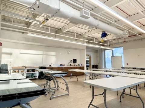 Multipurpose room with tables and chairs. A sink and counter can be seen on the far left wall.