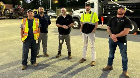 Five members of the Raleigh Water team stand for the camera. Truck with water pipes for Western NC is in the background.