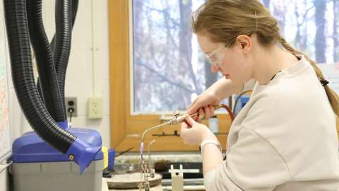 Young woman with blond hair wearing safety googles working with a torch to make jewelry