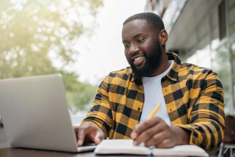 Man taking notes, looking at computer