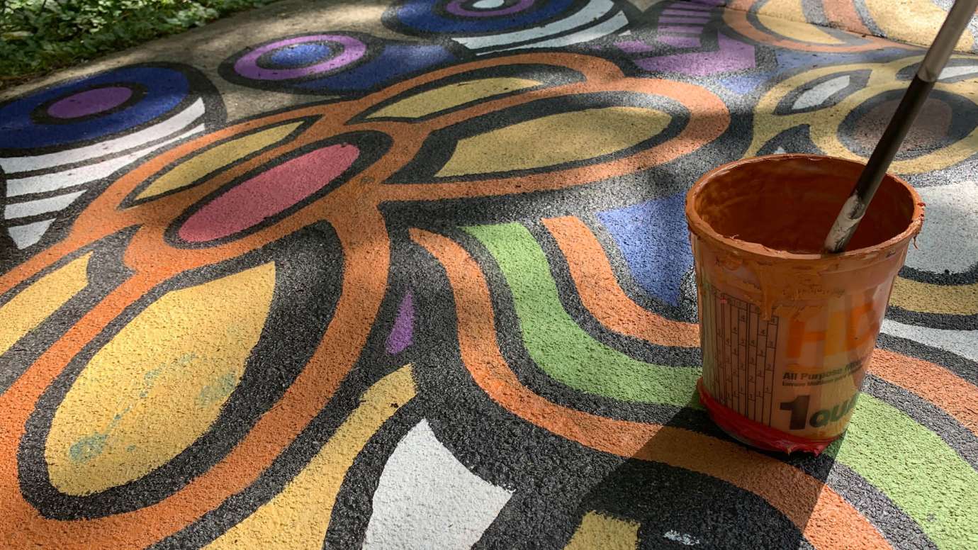 A storm drain and sidewalk mural on Chavis Way with orange, yellow, purple, blue, and white flowers and waterdrops