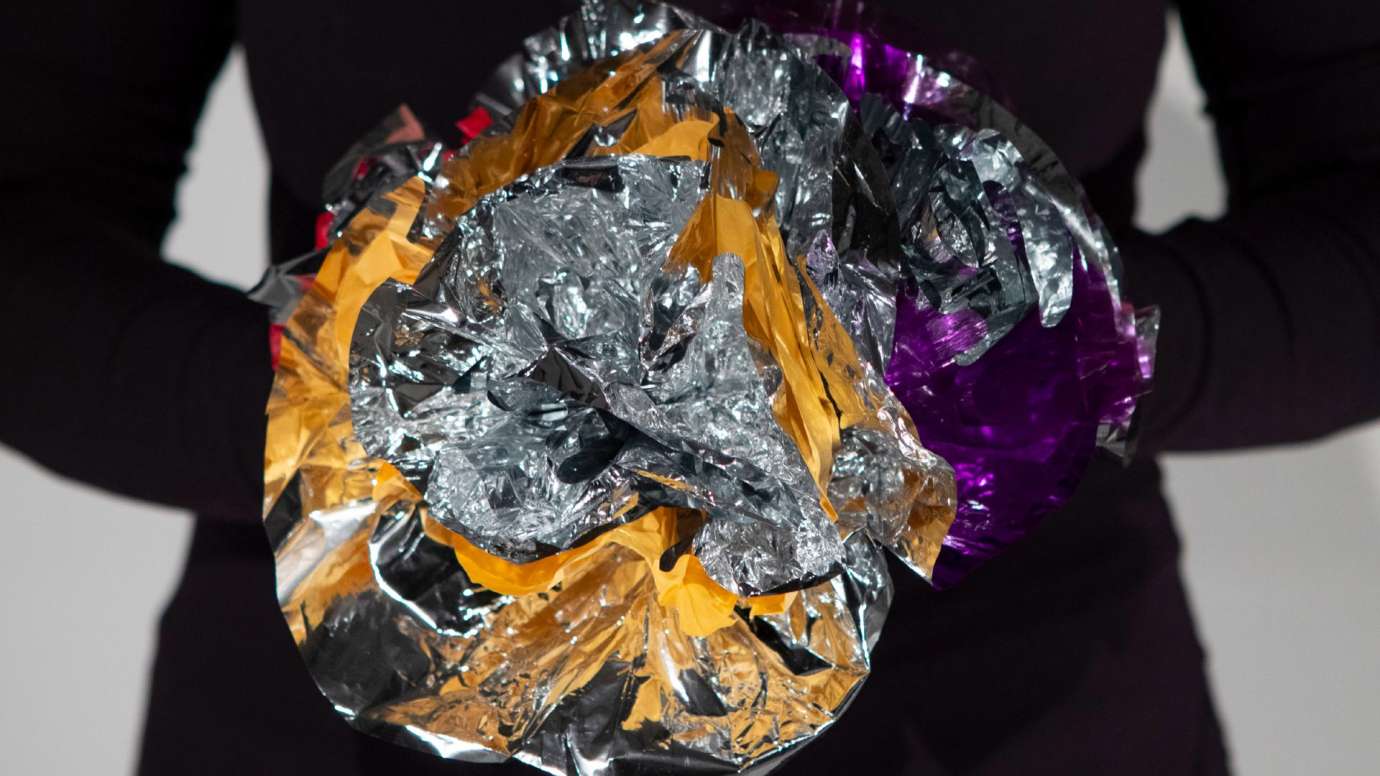 person holding a silver, gold, and purple mylar flower