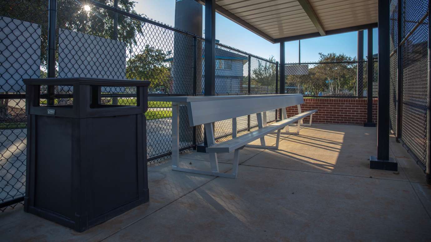 Inside of the enclosed and covered dugouts with a bench and trash can