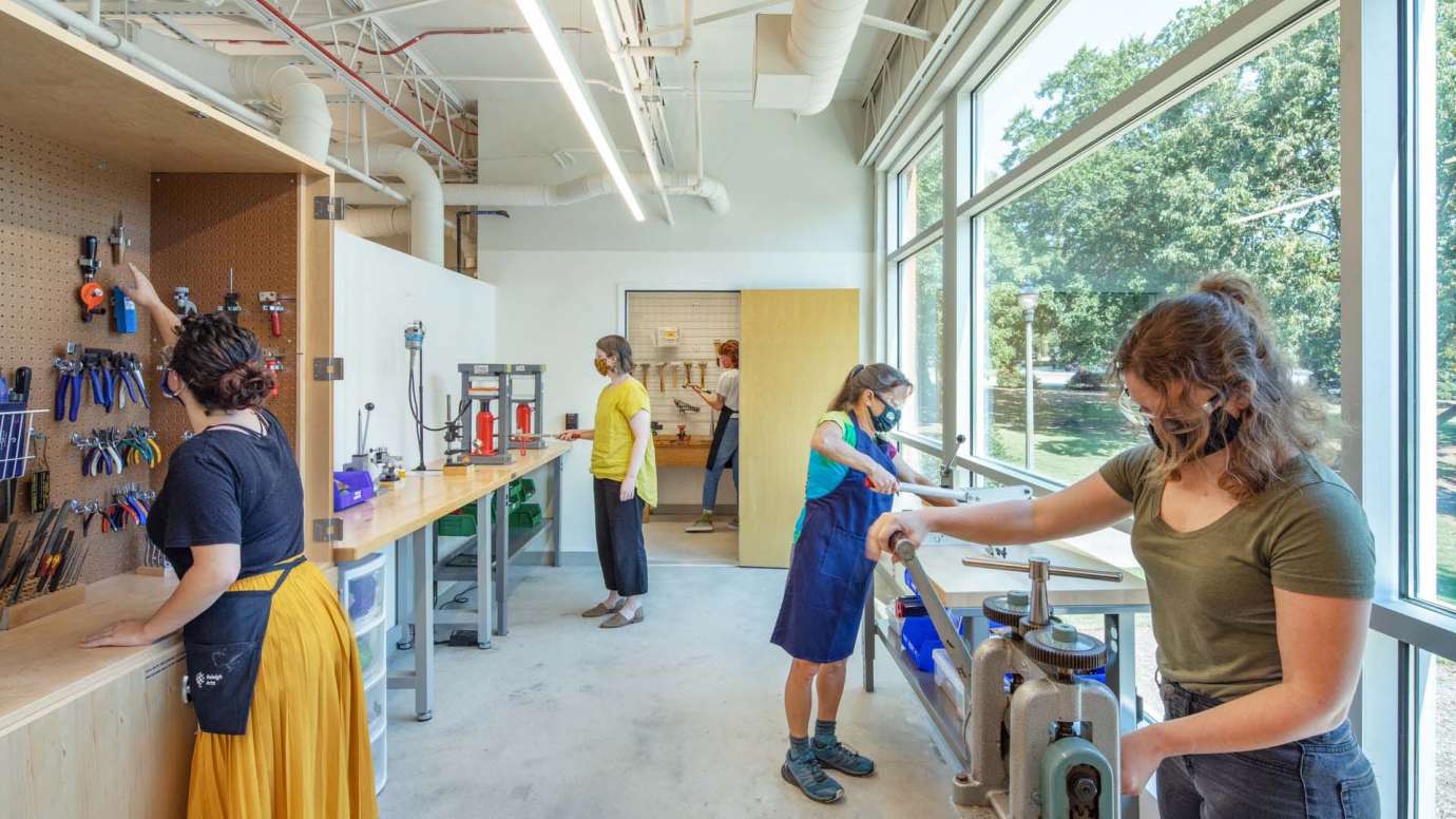 People using machinery and getting tools from a cabinet and closet in the jewelry studio at Pullen Arts Center