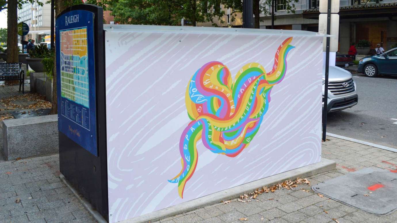 Artwork on a news rack kiosk that features a heart made from tangled rainbow ribbon that says pride and love on it