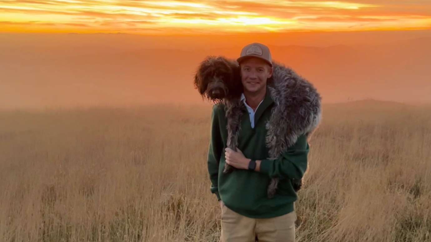 Man smiling with dog on shoulders in field