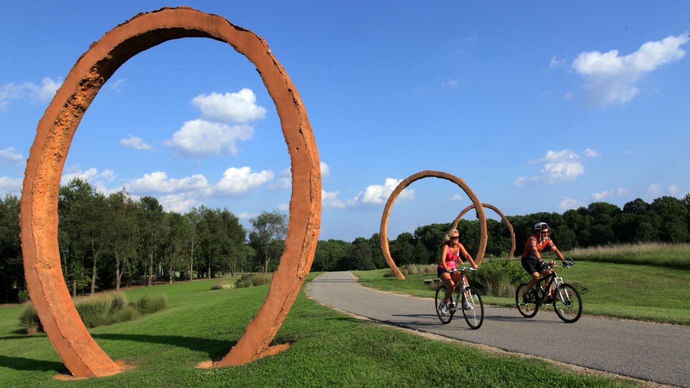 Two bikers ride through sculpture garden