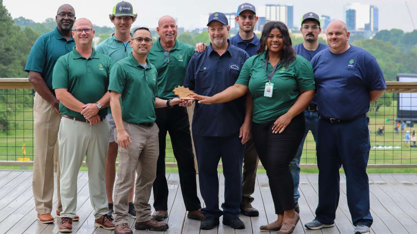 Raleigh's Vehicle Fleet Services team poses with the award with Raleigh skyline in background.