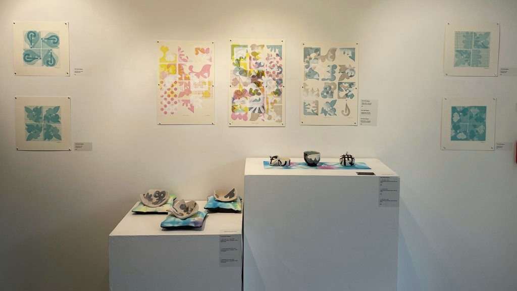 A display of ceramics and artwork on paper in muted but colorful blues, teals, greens and pinks. 