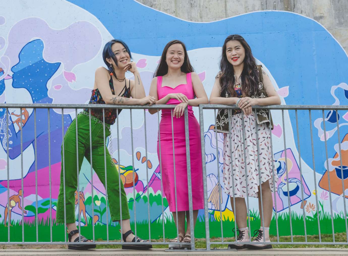 Three young Asian American women standing in front of a colorful mural