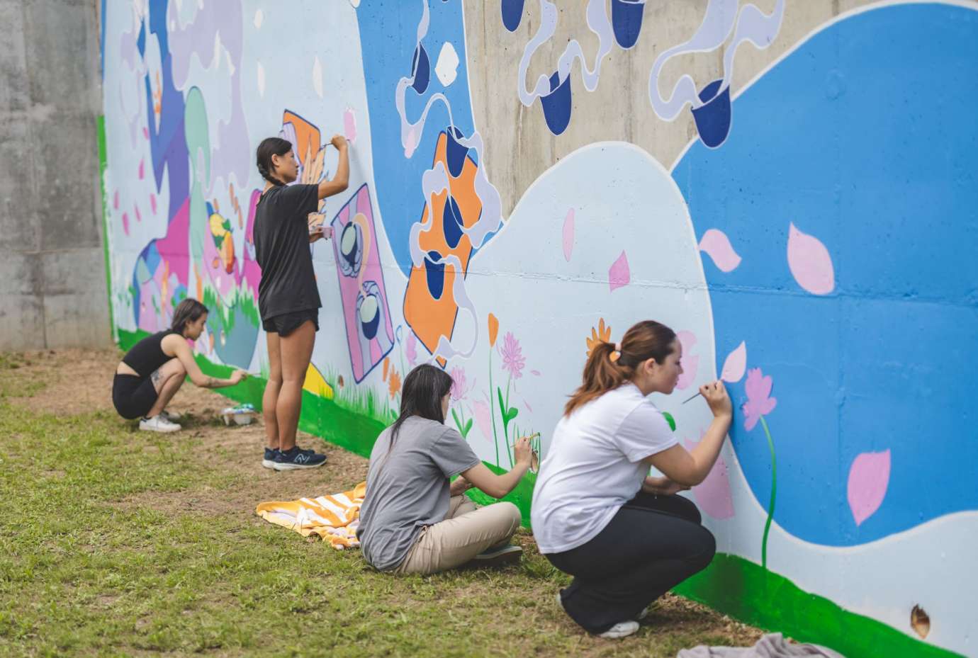 A group of people painting a colorful mural on a cement wall featuring an undulating wave figure