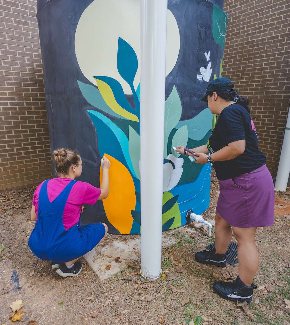 Artist and a helper painting a vertical cistern