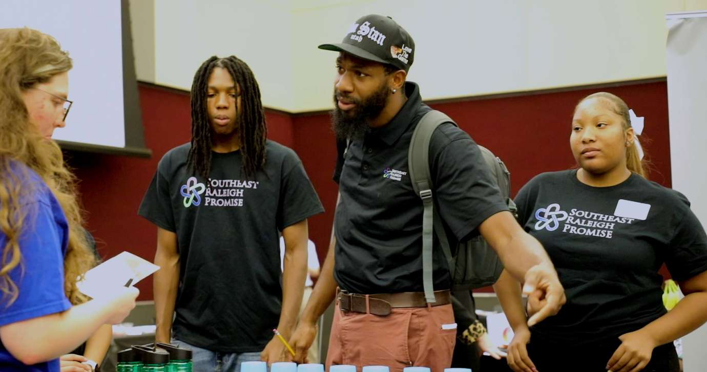 Three staff from Southeast Raleigh Promise speak to individual in the expo hall