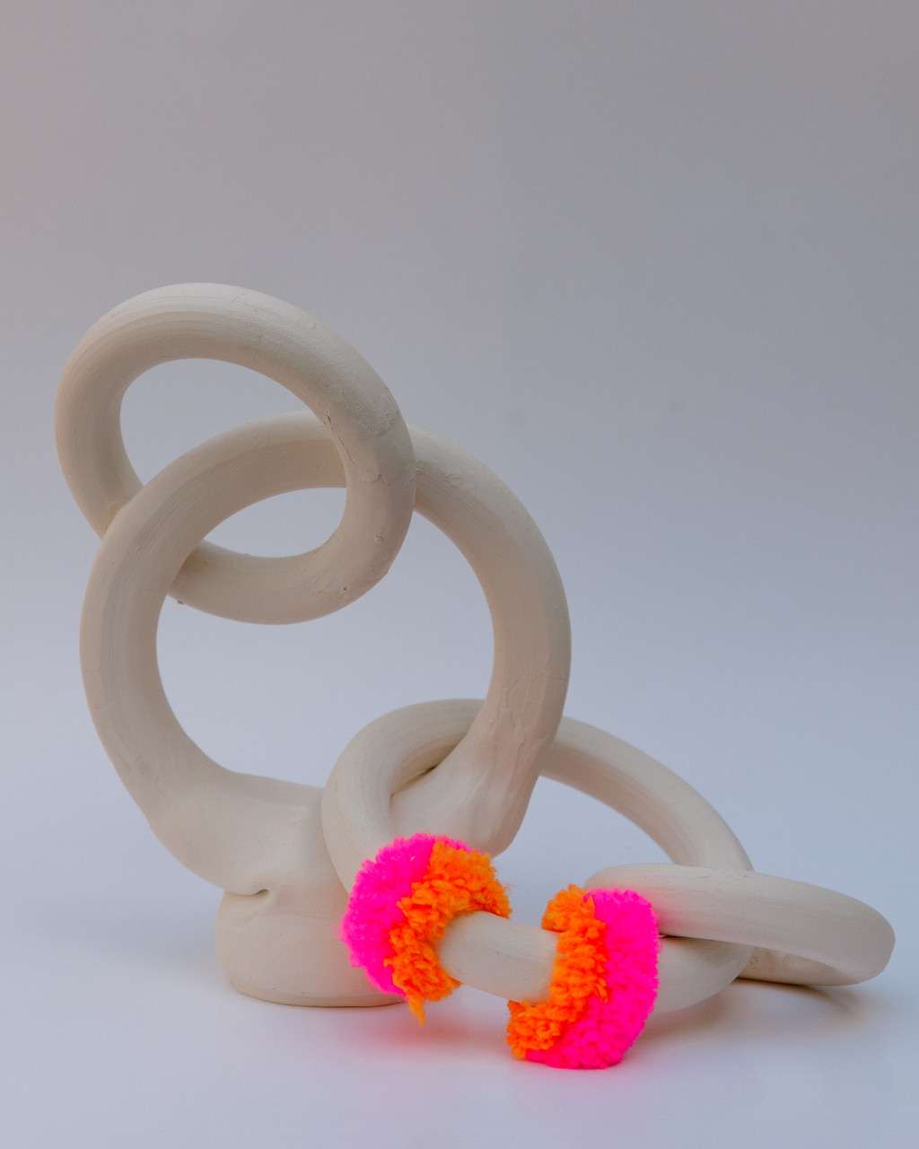 White ceramic sculpture of interconnected white rings with four rings of brightly colored yarn at the bottom.