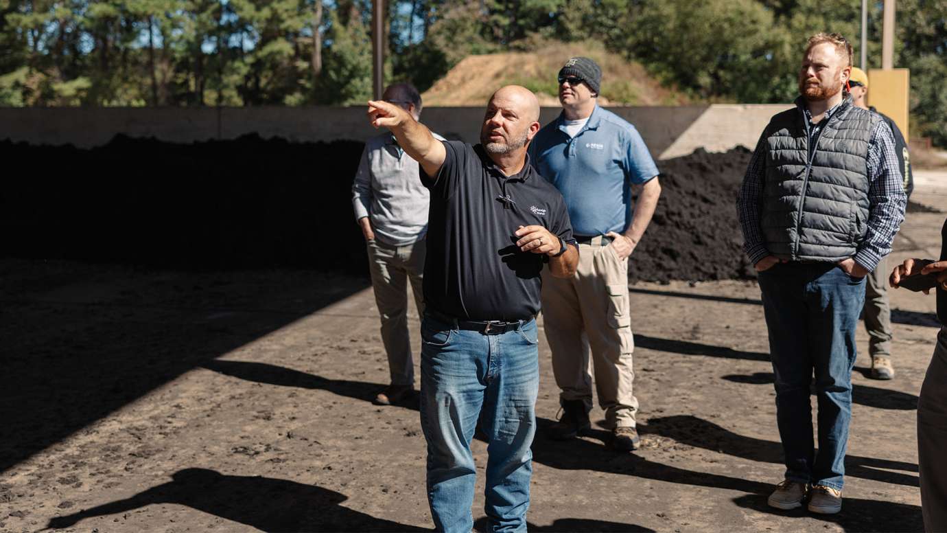 Man talking to tour group about the pile of black waste in front of them.