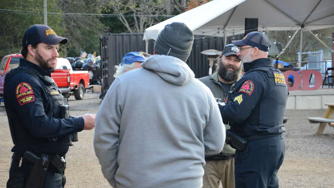 Two Raleigh police officers speaking to two men in Black Mountain with debris behind them