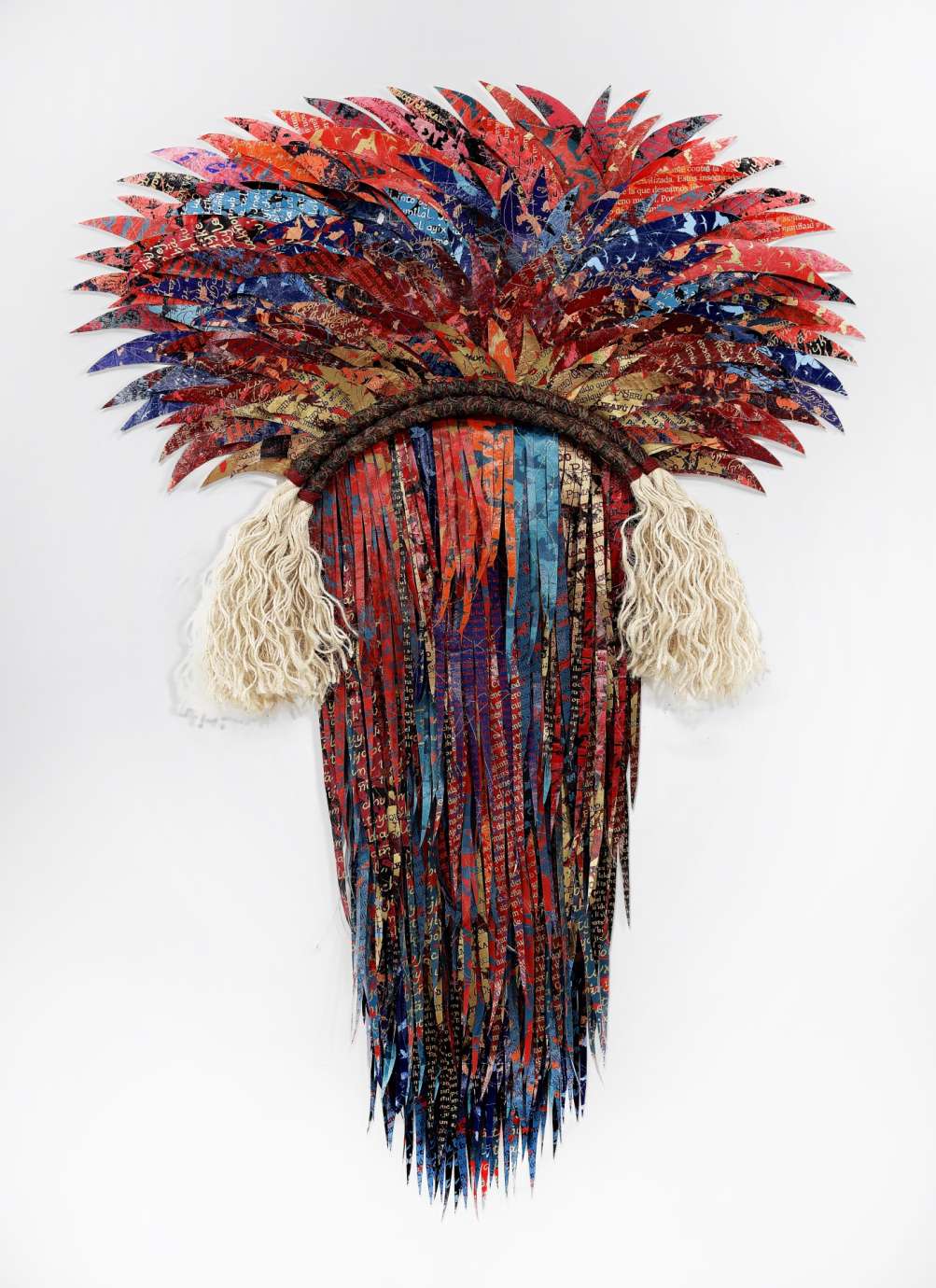 Two dimensional fiber sculpture with feather like fabric making a head-like shape in blues and reds. 