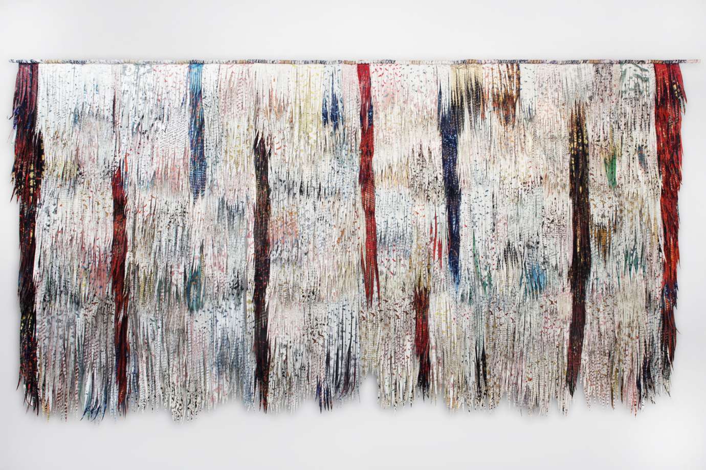 Two dimensional fiber sculpture with feather like fabric making a large white,  rectangular wall hanging with blue, red and purple line markings. 