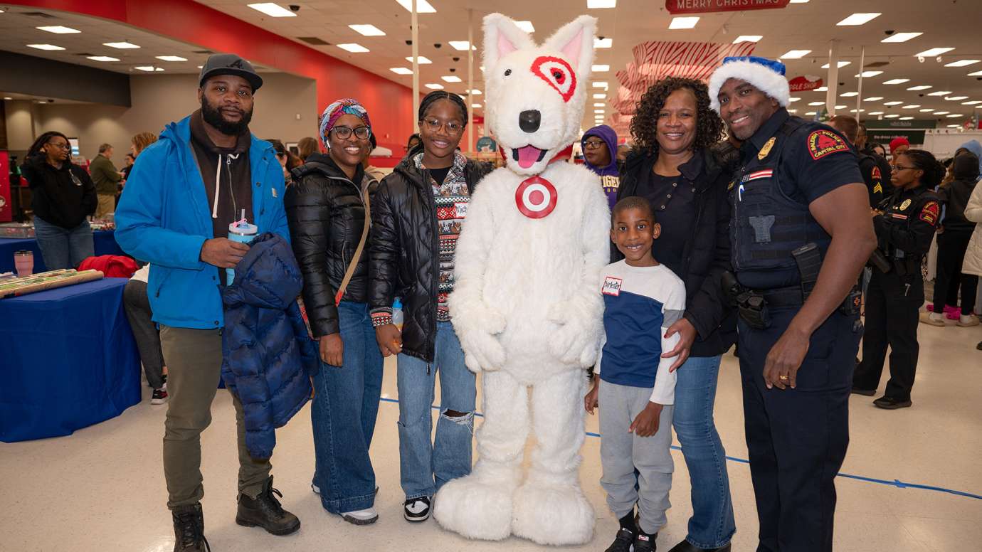 An officer, a child, and several adults gather around the Target dog mascot to pose for the photo.