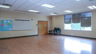 A large open multi-purpose room with a bulletin board and white board 