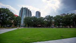 A view of part of the open lawn at Moore Square with the city buildings in the background 