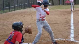 Kid at plate hitting baseball with catcher behind him