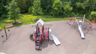 A large rubber surface playground with swings, slides and a climbing structure 